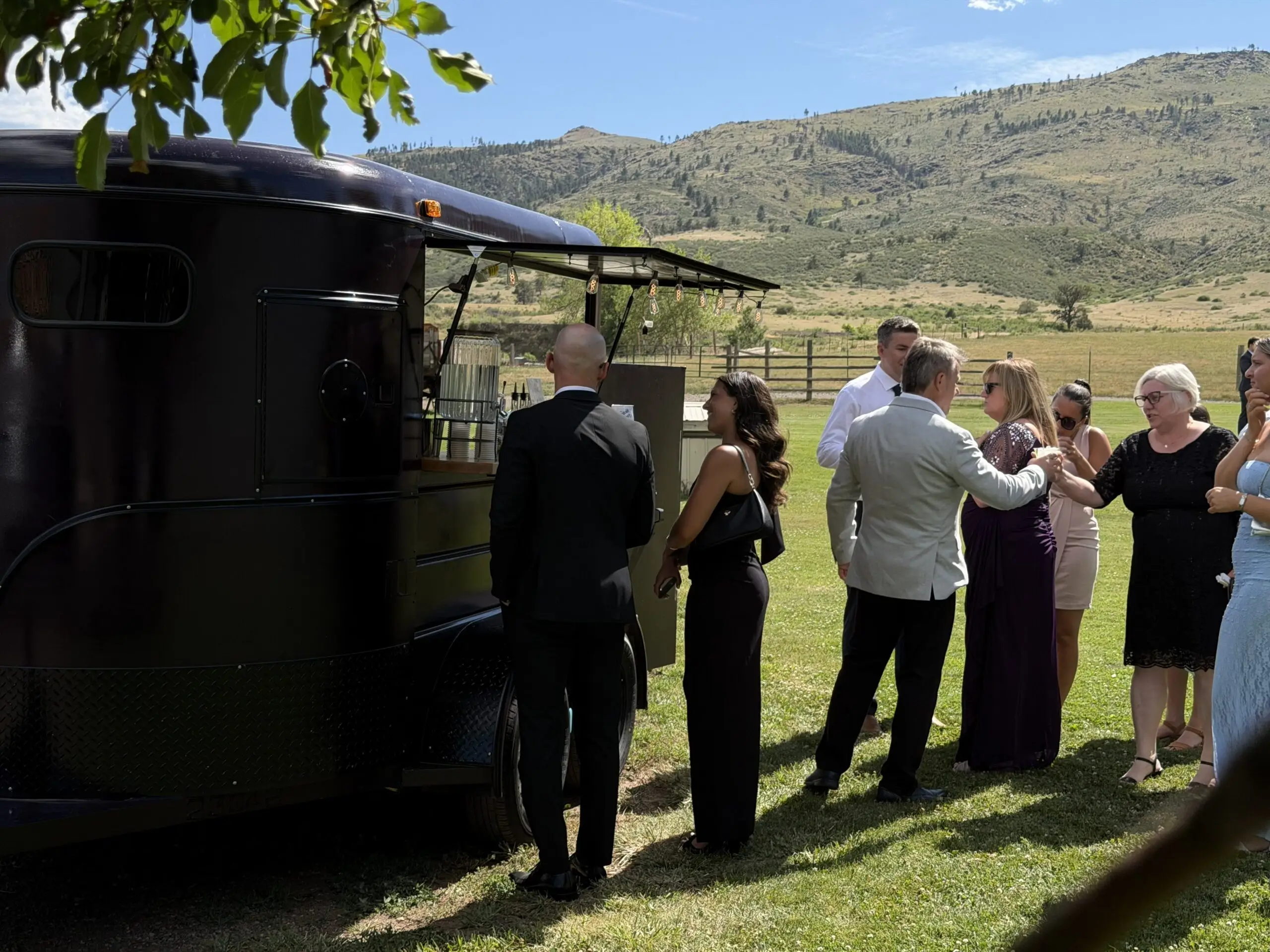Guests in formal attire gathered around The Portable Pour trailer bar at a mountain ranch wedding
